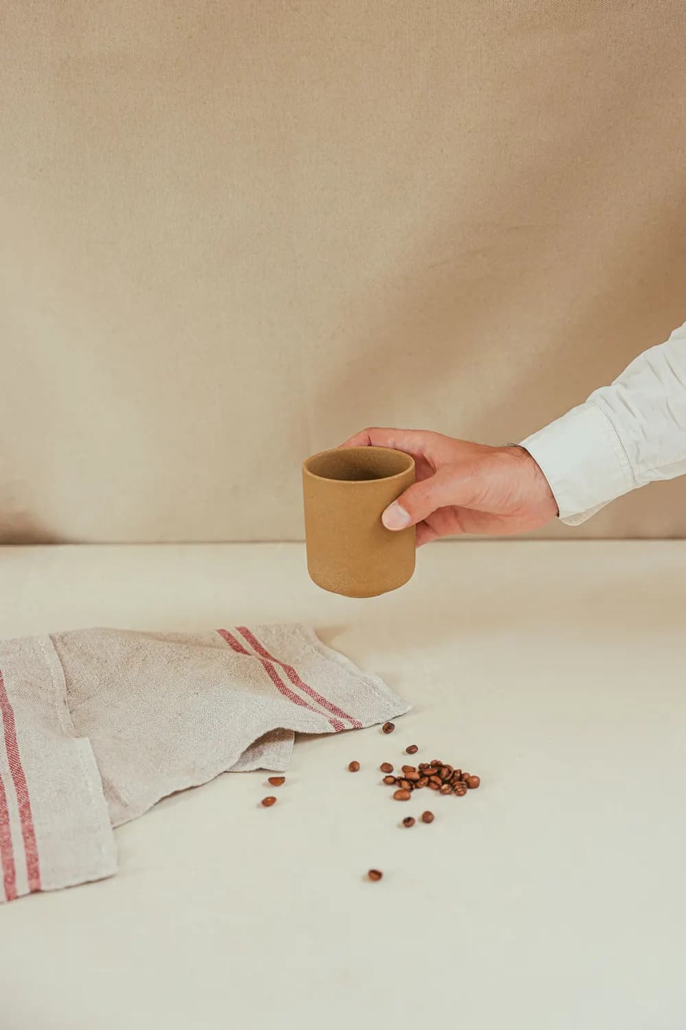 A hand holding a ceramic cup above scattered coffee beans