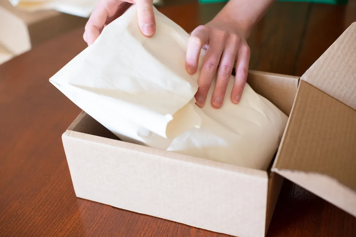 Des mains plaçant un paquet emballé dans un carton sur une table en bois