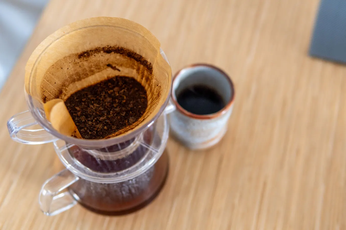 Un dripper pour-over avec du marc à côté d’une petite tasse de café filtre.