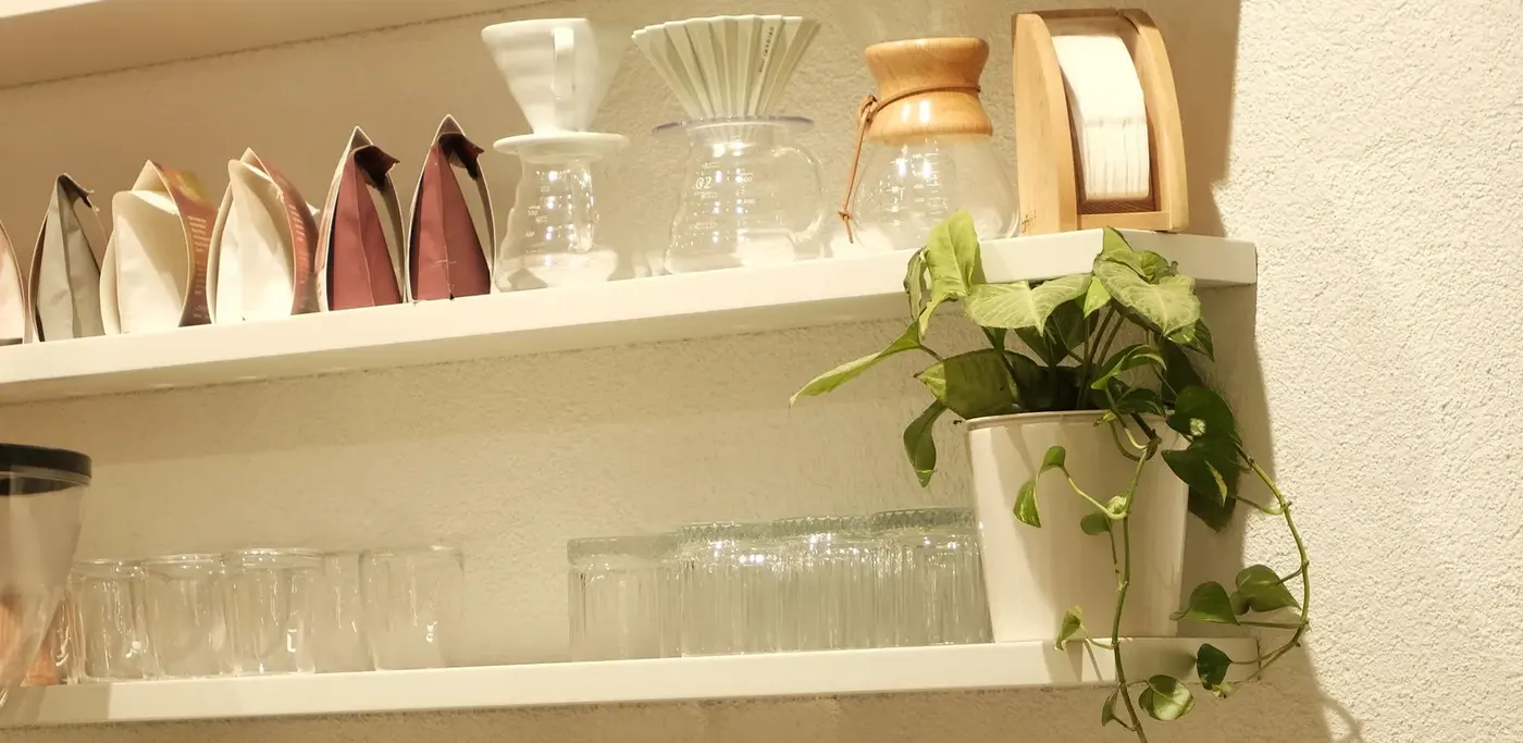 Coffee bags, pour-over brewers and glasses on the shelves of a coffee shop.